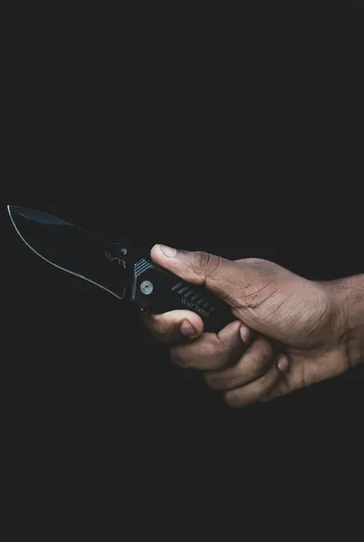 Mano sosteniendo una navaja plegable abierta sobre fondo oscuro con el filo en primer plano
